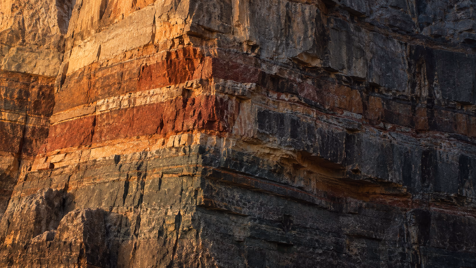 A quarry face in warm section: red, amber and ochre beds stacked against darker rock.